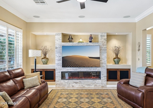 living room with built in features, ceiling fan, a stone fireplace, and ornamental molding