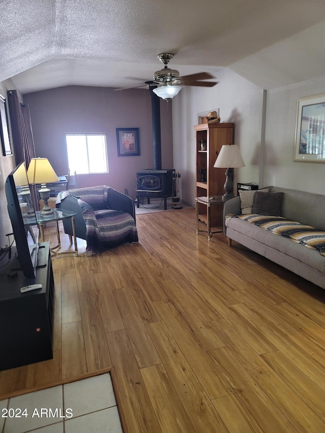 living room with a textured ceiling, ceiling fan, wood-type flooring, a wood stove, and lofted ceiling