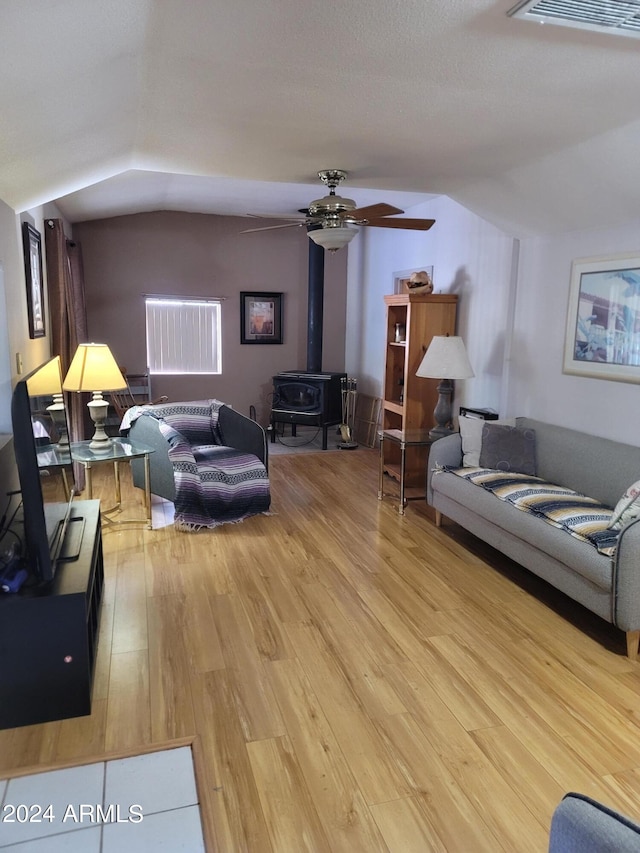 living room featuring light hardwood / wood-style floors, a wood stove, ceiling fan, and lofted ceiling