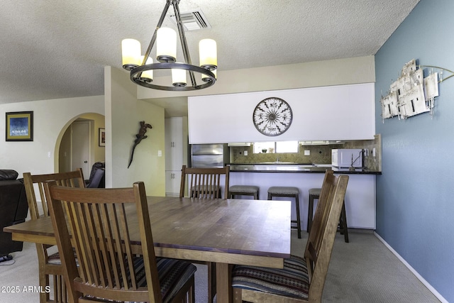 dining space featuring visible vents, an inviting chandelier, arched walkways, a textured ceiling, and light carpet