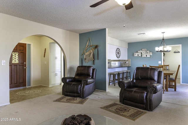 living area featuring visible vents, ceiling fan with notable chandelier, a textured ceiling, carpet floors, and arched walkways