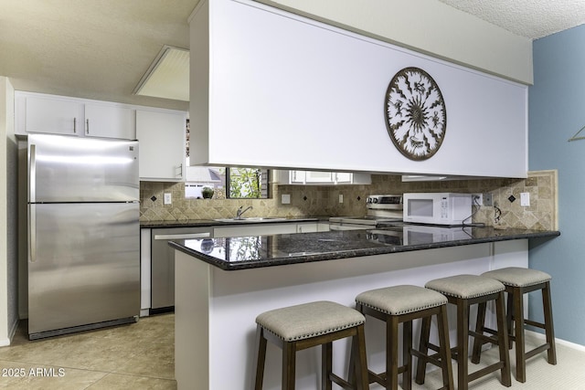 kitchen with backsplash, dark stone counters, appliances with stainless steel finishes, white cabinetry, and a sink