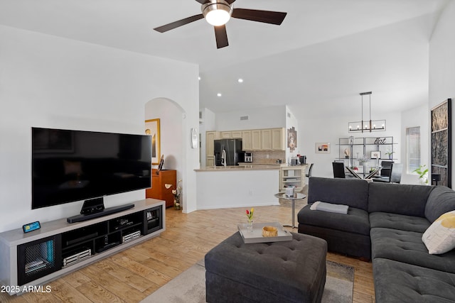living room with vaulted ceiling, ceiling fan with notable chandelier, arched walkways, light wood finished floors, and recessed lighting