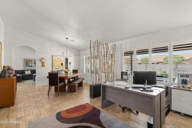 home office with arched walkways, light wood-style floors, lofted ceiling, and plenty of natural light
