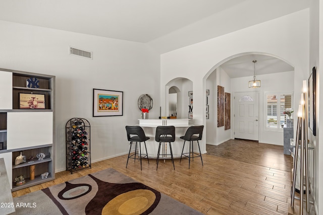 foyer entrance with wood finished floors, visible vents, arched walkways, baseboards, and high vaulted ceiling