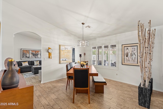 dining area with vaulted ceiling, arched walkways, light wood finished floors, a notable chandelier, and visible vents