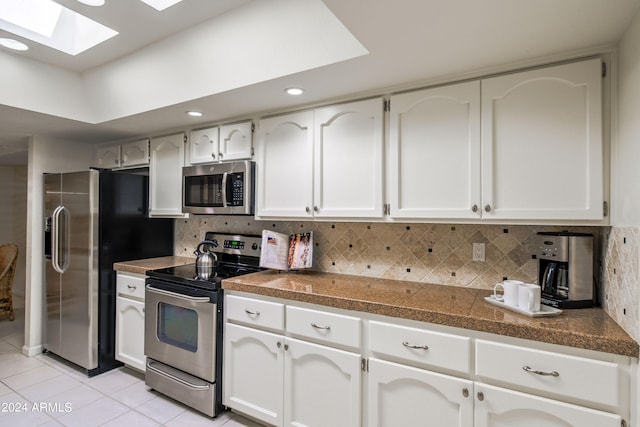 kitchen with white cabinets, decorative backsplash, a skylight, and stainless steel appliances