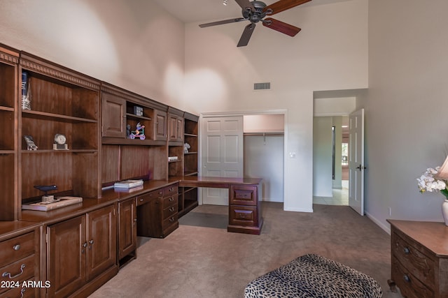 carpeted home office featuring a high ceiling, ceiling fan, and built in desk