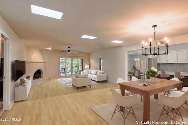 dining area featuring light hardwood / wood-style floors, ceiling fan with notable chandelier, and a large fireplace