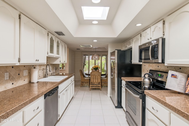 kitchen featuring white cabinetry, a skylight, stainless steel appliances, sink, and a raised ceiling