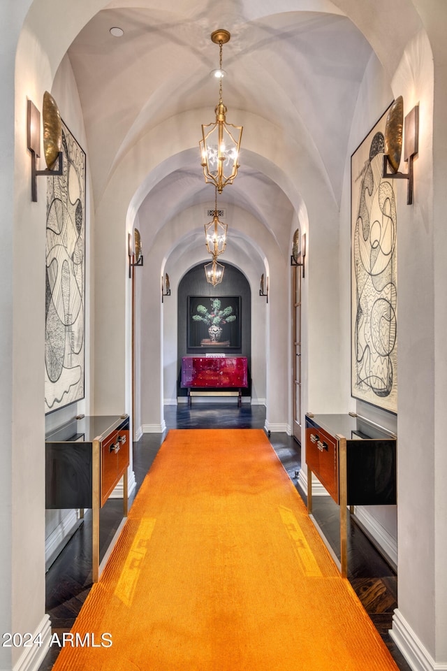 hall with baseboards, arched walkways, an inviting chandelier, and vaulted ceiling