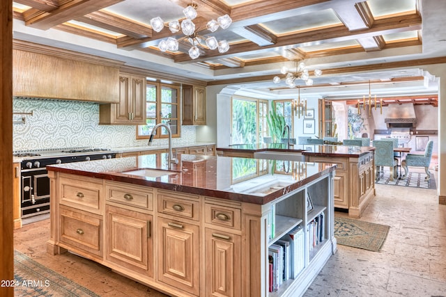 kitchen with a center island with sink, a sink, coffered ceiling, range with two ovens, and a chandelier