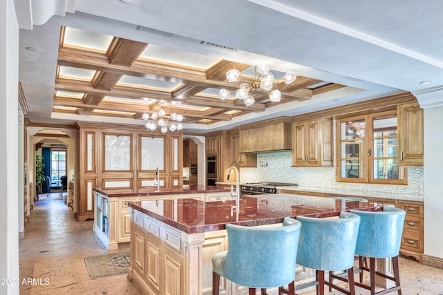 kitchen featuring tasteful backsplash, a center island with sink, an inviting chandelier, arched walkways, and coffered ceiling