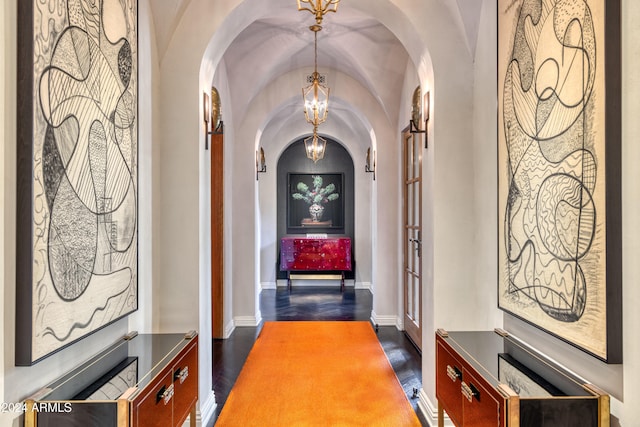 hall featuring baseboards, a chandelier, lofted ceiling, dark wood-style floors, and arched walkways