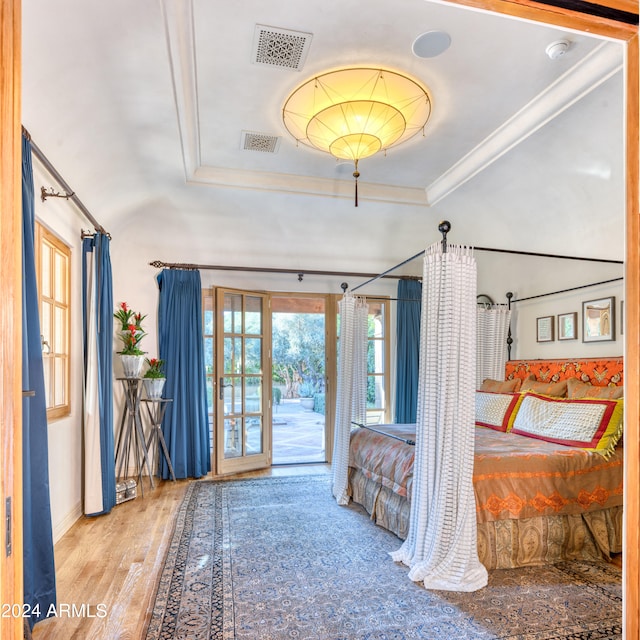 bedroom featuring access to exterior, visible vents, a tray ceiling, and wood finished floors