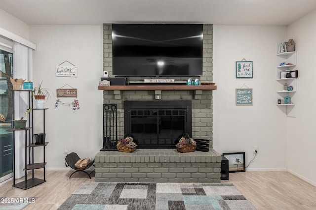 living room featuring a brick fireplace, baseboards, and wood finished floors