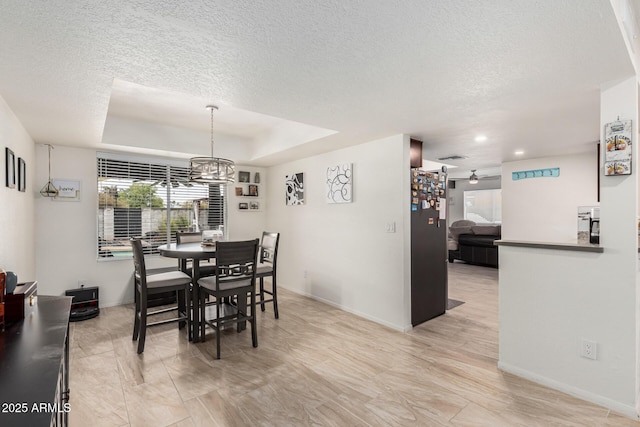 dining space featuring a textured ceiling, a raised ceiling, baseboards, and a ceiling fan