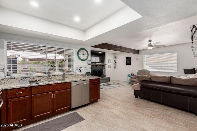 kitchen featuring dishwasher, light stone countertops, open floor plan, and a sink