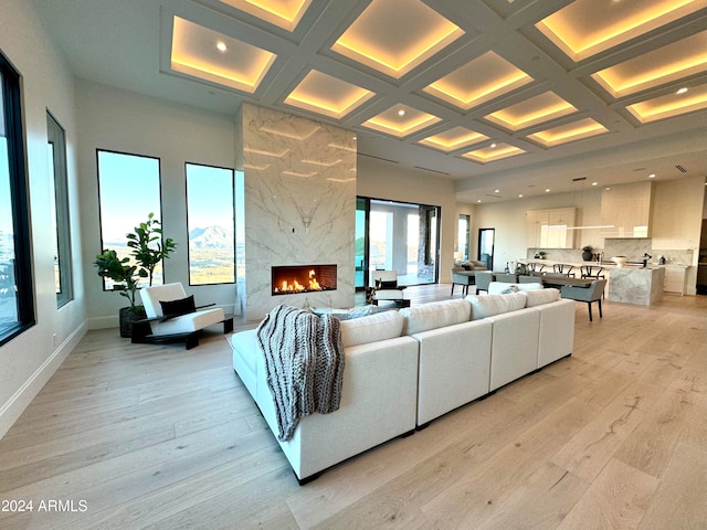 living room with light wood-style floors, a high ceiling, a high end fireplace, and coffered ceiling