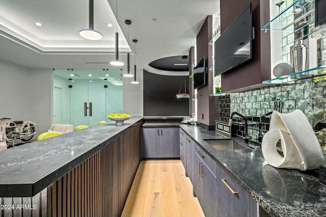 kitchen with dark stone countertops, sink, pendant lighting, and light hardwood / wood-style floors