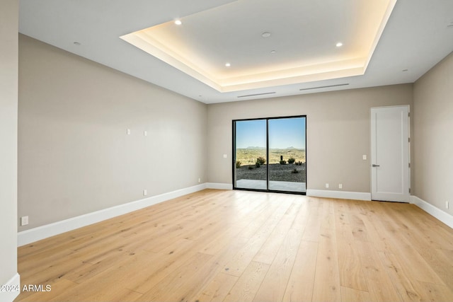 spare room with a tray ceiling and light hardwood / wood-style flooring