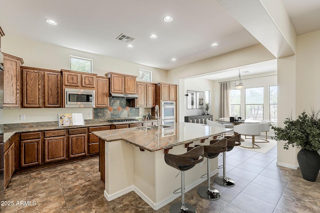 30374 N 124th Dr, Peoria, AZ 85383 - kitchen with stainless steel microwave, gas stovetop, a sink, a center island with sink, and light stone counters