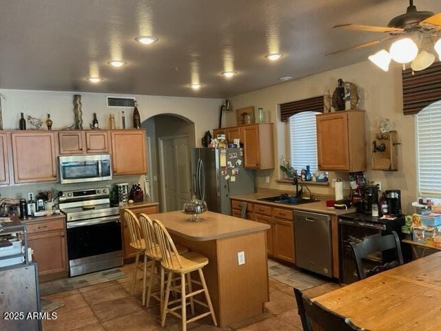 kitchen with appliances with stainless steel finishes, a breakfast bar, ceiling fan, sink, and a center island