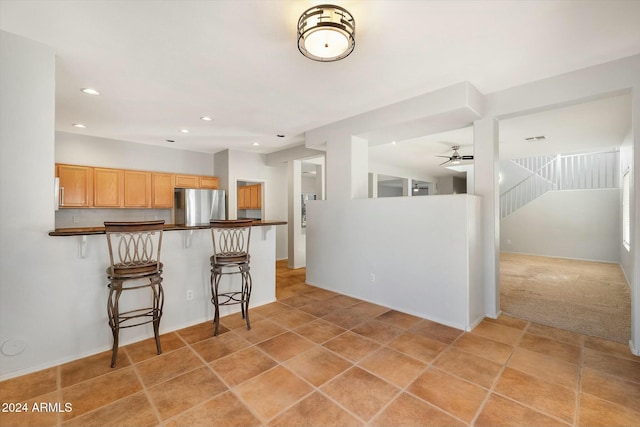 kitchen featuring kitchen peninsula, stainless steel fridge, light colored carpet, ceiling fan, and a breakfast bar area