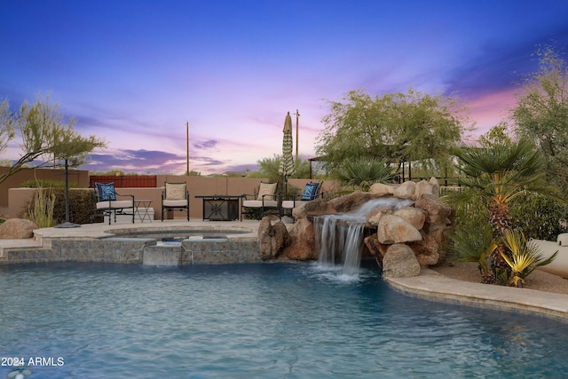 pool at dusk featuring pool water feature and an in ground hot tub