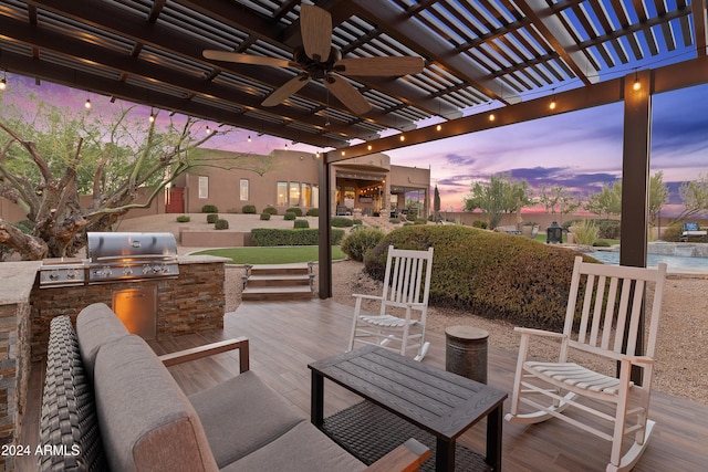 patio terrace at dusk with outdoor lounge area, a pergola, ceiling fan, a grill, and exterior kitchen