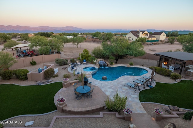 pool at dusk with pool water feature, a patio area, and a yard