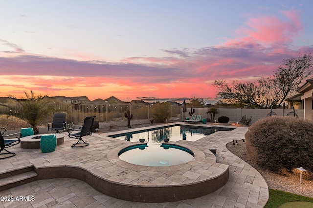 pool at dusk featuring an in ground hot tub, a patio, and an outdoor fire pit