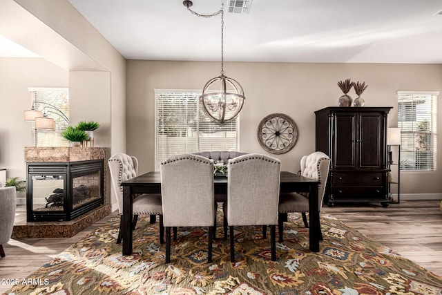 dining area with an inviting chandelier, wood-type flooring, a healthy amount of sunlight, and a multi sided fireplace