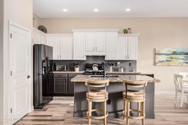 kitchen with black fridge, an island with sink, decorative backsplash, and white cabinets