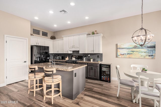 kitchen featuring sink, a kitchen island with sink, light stone counters, black appliances, and white cabinets