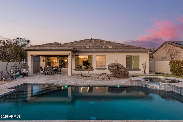 back house at dusk with a swimming pool with hot tub and a patio