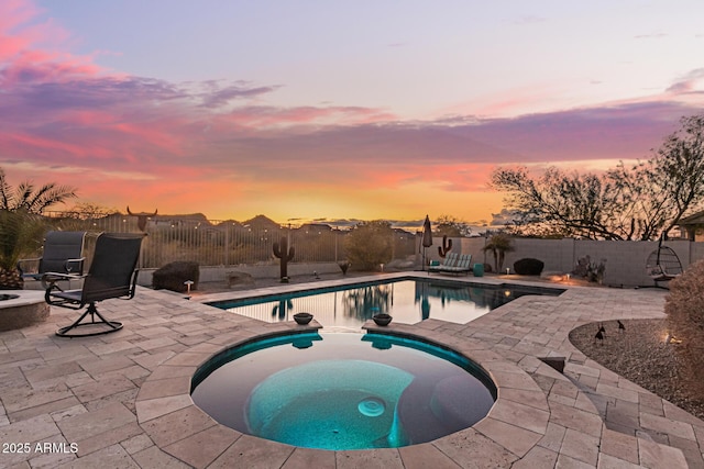 pool at dusk with an in ground hot tub and a patio area