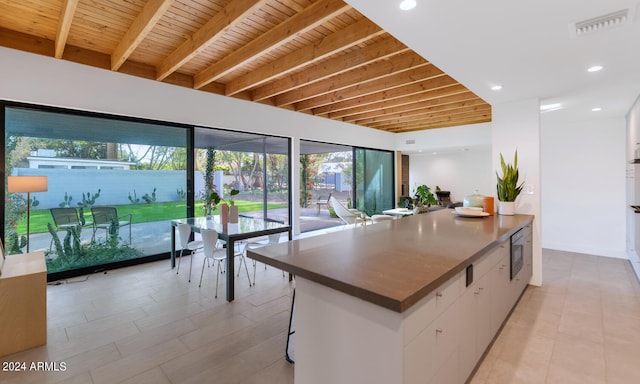 kitchen featuring a breakfast bar, stainless steel microwave, wooden ceiling, white cabinets, and beamed ceiling