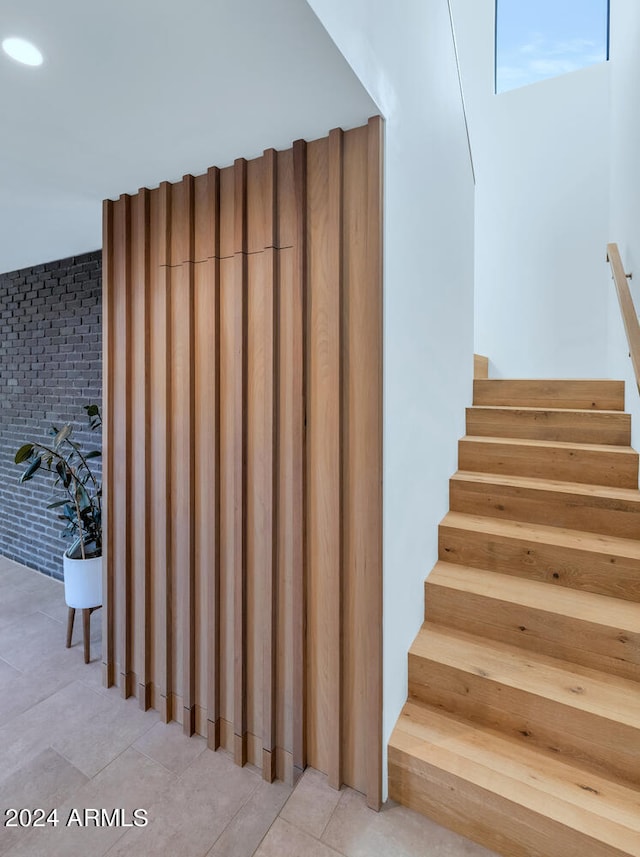 stairs with tile patterned flooring and brick wall