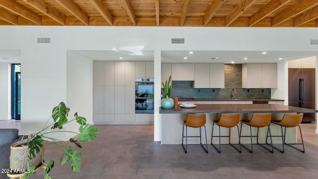 kitchen featuring beamed ceiling, a kitchen bar, decorative backsplash, stainless steel built in fridge, and white cabinets