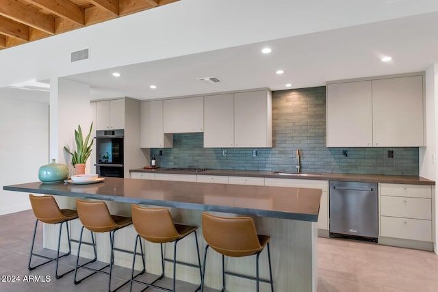 kitchen with decorative backsplash, appliances with stainless steel finishes, a kitchen breakfast bar, sink, and a center island