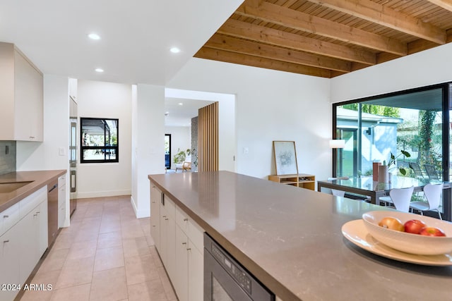 kitchen featuring stainless steel dishwasher, wood ceiling, sink, beam ceiling, and white cabinetry