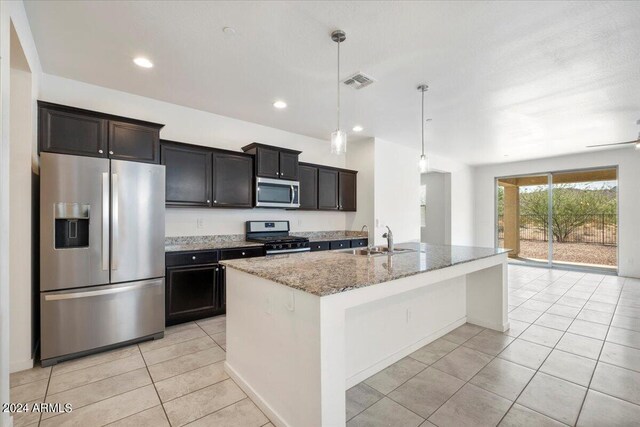 kitchen with light tile patterned floors, light stone counters, appliances with stainless steel finishes, decorative light fixtures, and sink