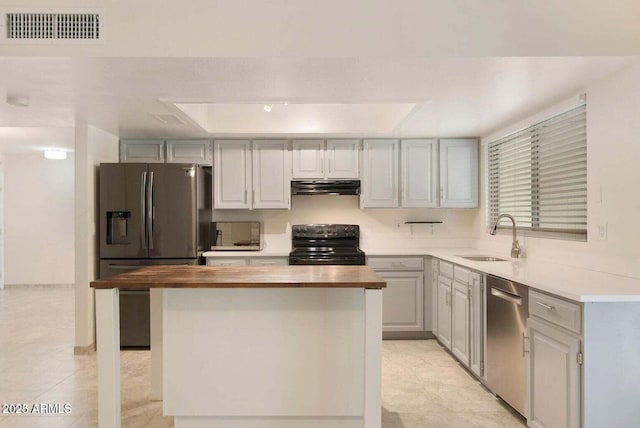 kitchen with appliances with stainless steel finishes, butcher block countertops, sink, gray cabinetry, and a raised ceiling