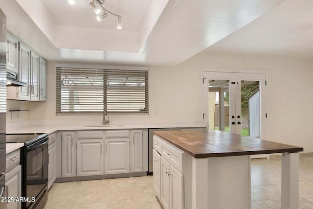 kitchen featuring butcher block countertops, black electric range oven, sink, a raised ceiling, and a healthy amount of sunlight