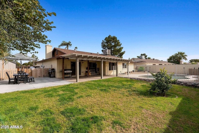 rear view of property with a fenced in pool, a patio area, and a lawn