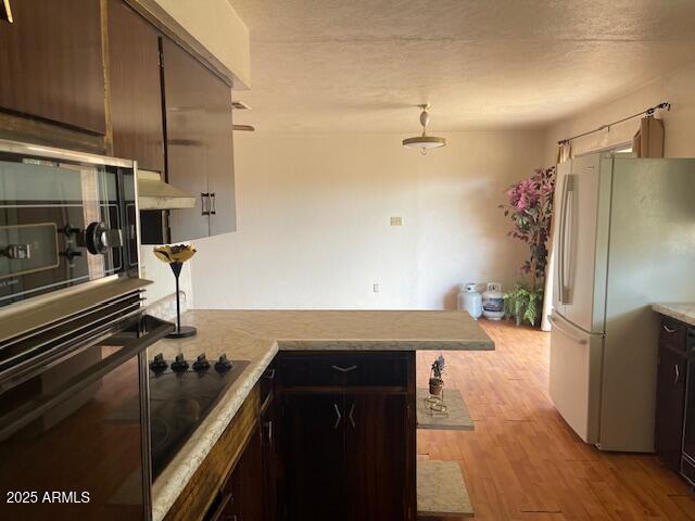 1010 N Florida Ave, Douglas, AZ 85607 - kitchen featuring freestanding refrigerator, light wood-style flooring, a peninsula, light countertops, and black electric cooktop