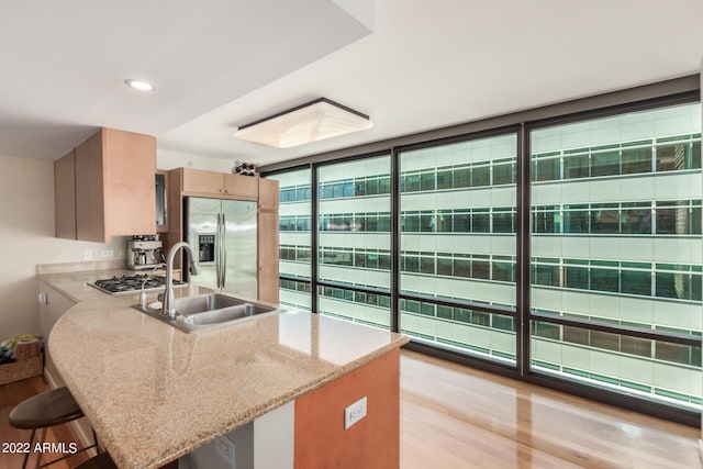 kitchen featuring floor to ceiling windows, stainless steel refrigerator with ice dispenser, light wood-type flooring, a breakfast bar, and sink