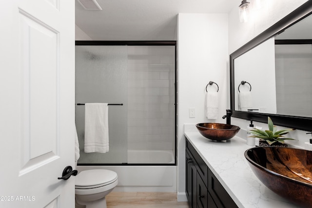full bathroom featuring double vanity, bath / shower combo with glass door, and toilet