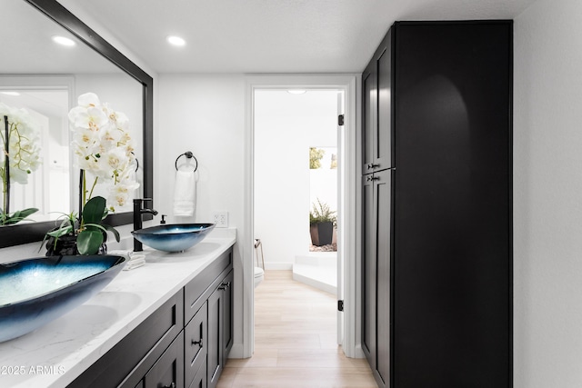 bathroom with toilet, recessed lighting, wood finished floors, and double vanity
